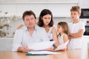 A family gathers in a kitchen and reviews paperwork while looking stressed out.