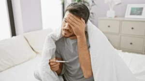 A man sick in bed with a fever. You can work with a lawyer to learn more about the paid sick leave laws in Connecticut.